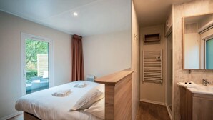 Un dormitorio con cama, ventana, baño con lavamanos y espejo, y un perchero para toallas.