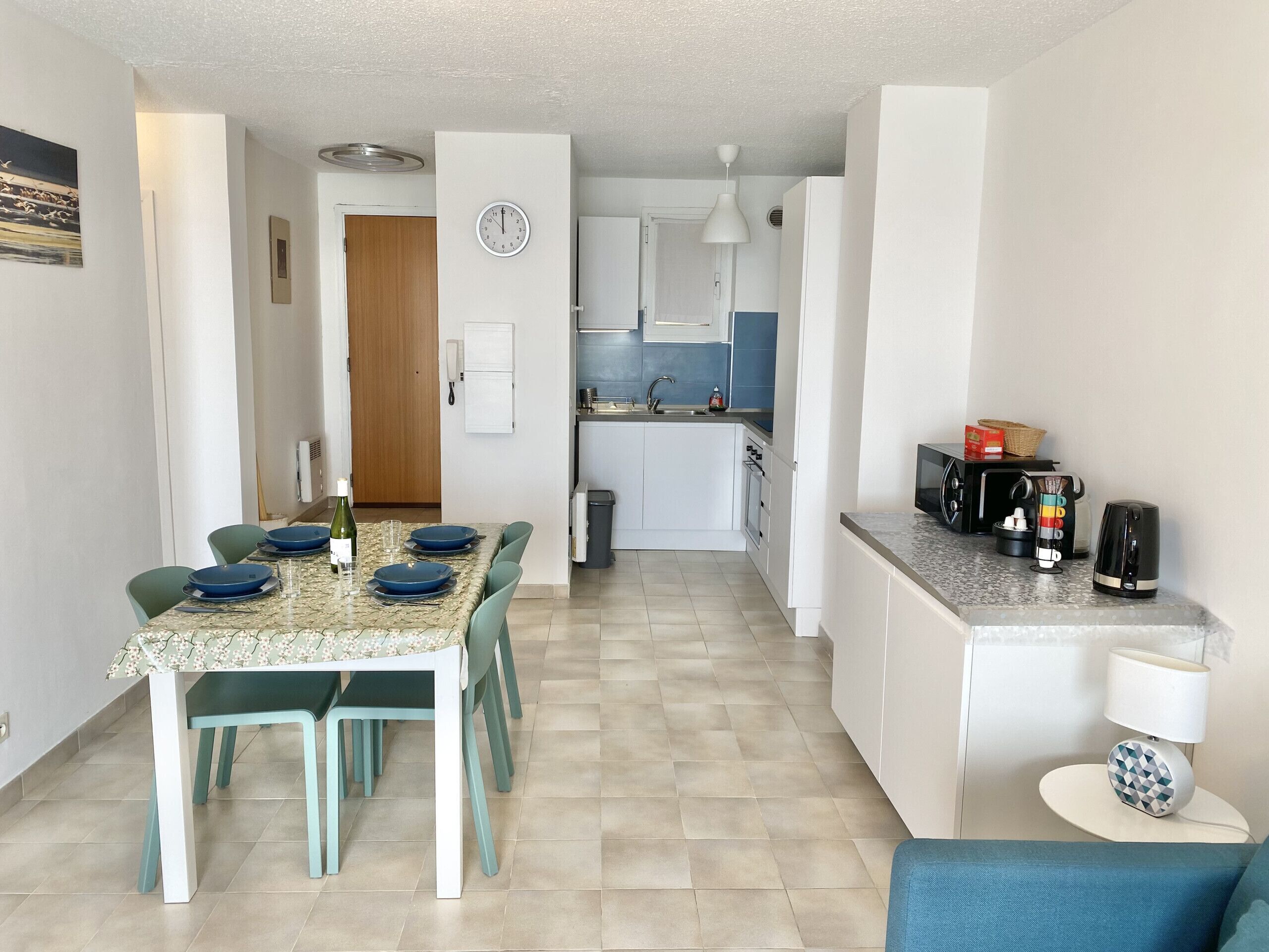 Cucina moderna con mobili bianchi, lavandino e forno a microonde. Un'area pranzo con un tavolo imbandito per due persone e sedie.