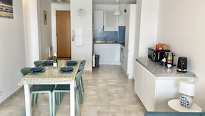 Una cocina moderna con armarios blancos, un fregadero y un microondas. Hay una zona de comedor con una mesa preparada para dos sillas.