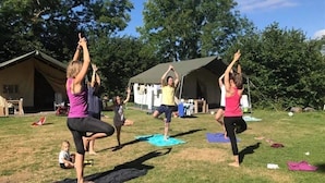 En gruppe mennesker dyrker yoga udendørs på en græsplæne med telte i baggrunden.