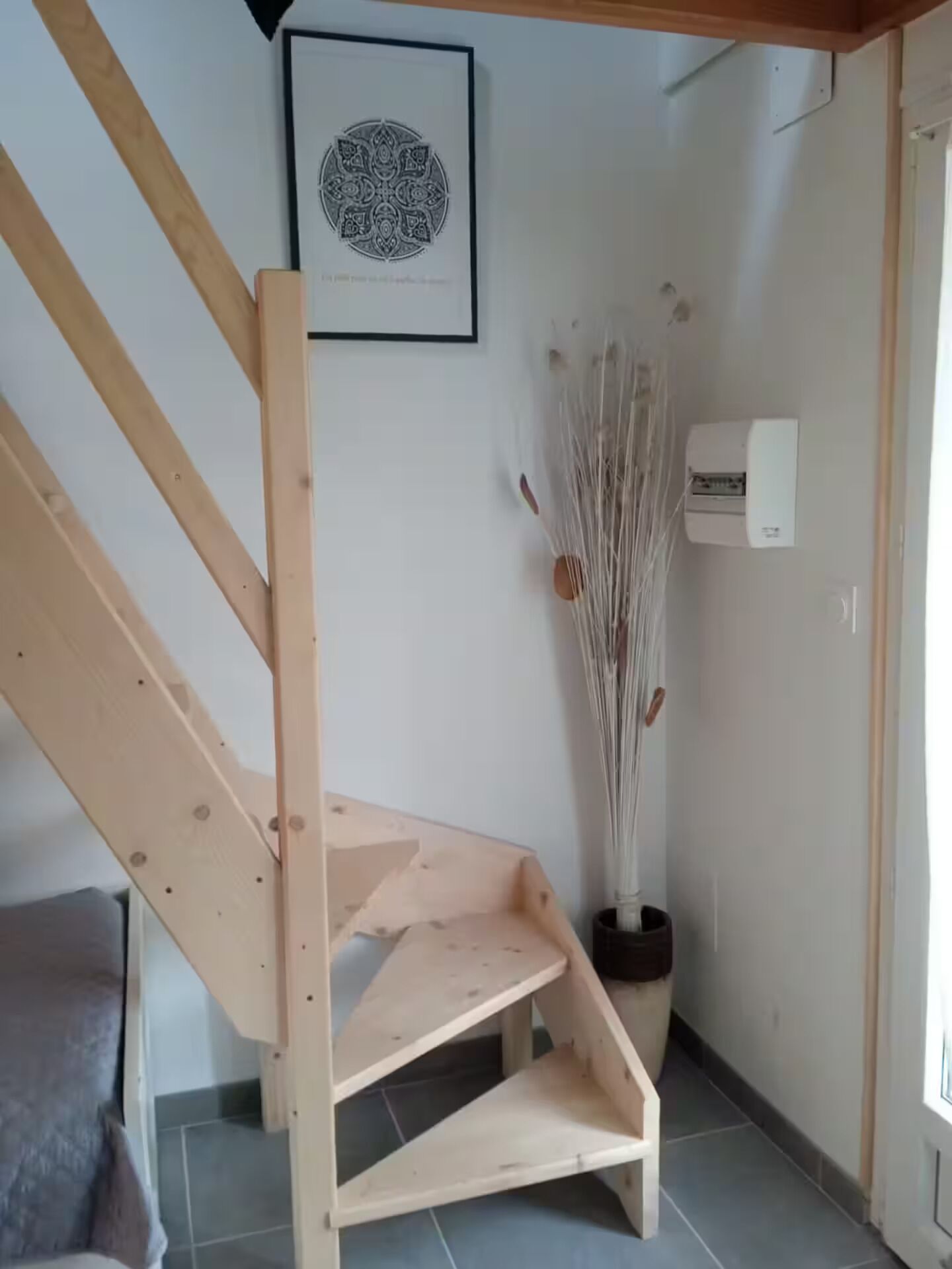 A wooden staircase with a simple design, a framed artwork on the wall, and a decorative plant in a black pot.