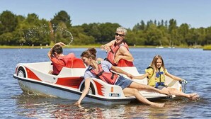 A small, open boat with four people wearing life jackets, floating on a calm lake.