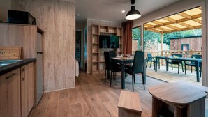 A modern kitchen with wooden cabinetry, a dining area with a table and chairs, and a view of an outdoor deck. - ZEcamping 5* parc aquatique club enfant fitness locatif BBQ 2 pers (Quimper)