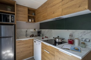 Et moderne køkken med træskabe, et rustfrit stål køleskab, en opvaskemaskine, en sort induktionskogeblus og en marmorbeklædt væg.