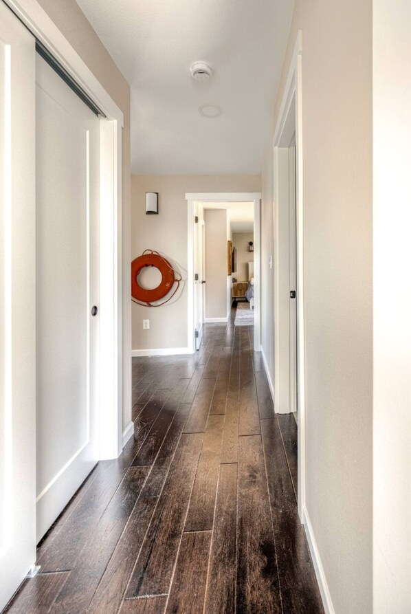 A hallway with dark wooden flooring, white walls, and a red fire safety device.
