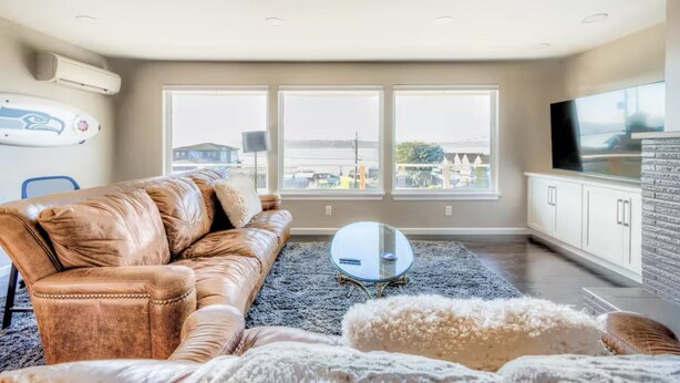 A modern living room with a leather sofa, a glass coffee table, and a view of the city through large windows. - Charming 2-bedroom unit with WiFi, AC with amazing Puget Sound view in Tacoma (Tacoma)