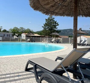 Una piscina amb gandules i ombrel·les, envoltada per una tanca i edificis.