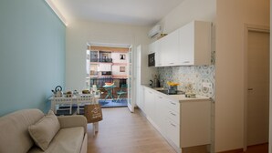 Un espace de vie compact comprenant un coin cuisine, un coin repas et donnant sur un balcon.