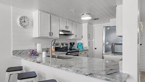 A modern kitchen with white cabinetry, a granite countertop, a built-in oven, and a coffee maker.
