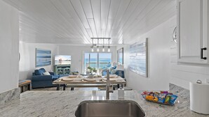 A modern kitchen with a granite countertop, stainless steel sink, and a dining area with a blue sofa and a table set for two.