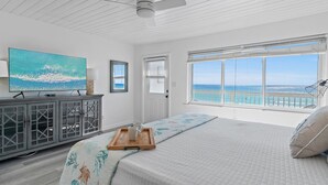 A bedroom with a large bed, a television, a cabinet, and a window with a view of the ocean.