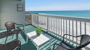 A balcony with wicker chairs, a white table, and a potted plant.