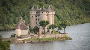 Un castillo con múltiples torres, un foso y un río al fondo.