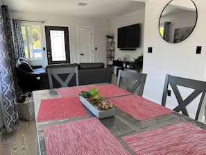 A dining area with a table set for four, surrounded by chairs, and a sofa in the background. - Oasis 2BR Culver City: 6 Miles to SoFi Stadium (Culver City)