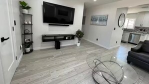 A modern living room with a flat-screen TV, a glass coffee table, and a grey sofa. - Cheerful house with EV, Parking & backyard (Culver City)