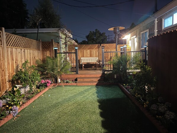 A backyard with a wooden fence, a lawn, and a patio area with a bench and table. - Oasis 2BR Culver City: 6 Miles to SoFi Stadium (Culver City)