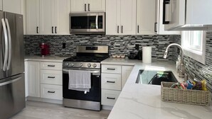 A modern kitchen with white cabinets, a stainless steel refrigerator, a microwave, a gas stove, and a sink. - Cheerful house with EV, Parking & backyard (Culver City)