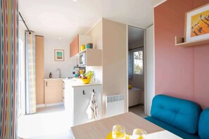 Uma sala de estar moderna com um sofá azul, uma mesa de jantar com copos e uma área de cozinha com micro-ondas e uma fruteira.