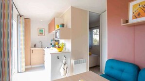Un salon moderne avec un canapé bleu, une table à manger avec des verres et un coin cuisine avec un saladier jaune rempli de fruits.