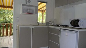Una cocina compacta con microondas, un refrigerador pequeño y un lavamanos. Hay una ventana que proporciona luz natural y vistas a la vegetación exterior.