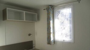 Un dormitorio con cama, mesita de noche, estante empotrado sobre la cama y ventana con cortinas estampadas.