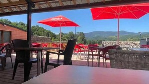 Un espacio de comedor al aire libre con mesas y sillas, sombrillas rojas y vistas a un paisaje montañoso.