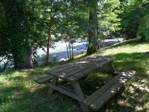 Ein Holztisch für ein Picknick in einer natürlichen Umgebung, im Hintergrund fließt ein Fluss.