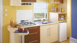 A compact kitchen with a gas stove, a sink, and a small refrigerator. There is a window providing natural light, and the walls are painted yellow.
