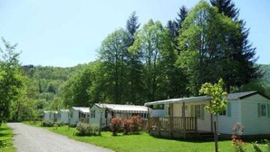 A row of mobile homes with a gravel road in front, surrounded by greenery and trees.