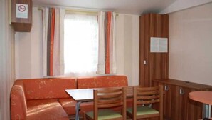 A compact room with a sofa, two wooden chairs, a small table, and a window with curtains.