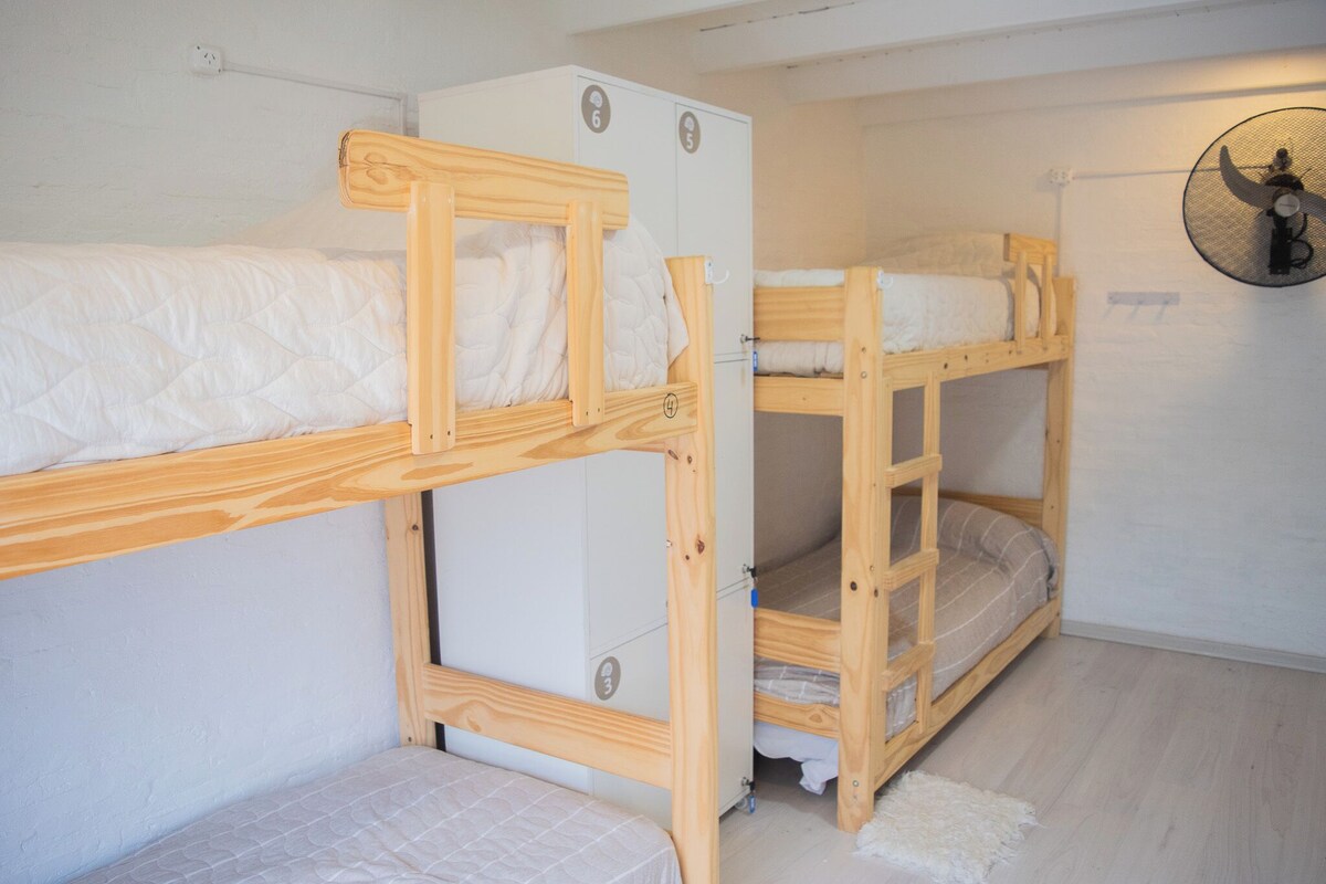 Une chambre de dortoir avec des lits superposés, une armoire blanche et un ventilateur de plafond.