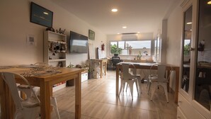 Una cocina amplia con piso de madera, un comedor con sillas blancas y un gran ventanal que proporciona luz natural.