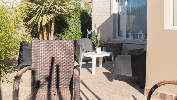 Un espacio al aire libre con sillas de mimbre, una mesa, una palmera y un edificio con un ventanal grande.