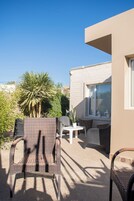 Un espacio al aire libre con sillas de mimbre, una mesa, una palmera y un edificio con un ventanal grande.