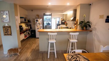 Una cocina con mostrador de madera, dos taburetes blancos, un gato y un perro.
