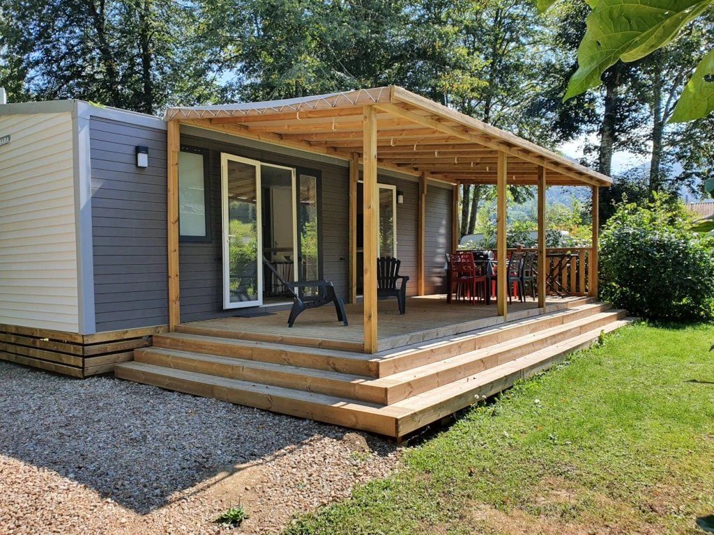Uma pequena cabana com um deck de madeira, um alpendre coberto e um caminho de acesso de cascalho.