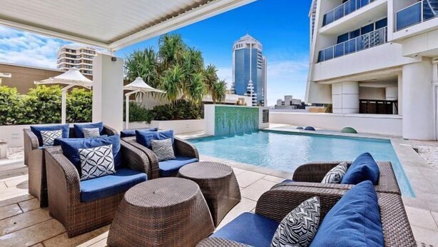 Zona de piscina en la azotea con mobiliario de mimbre y vistas a un edificio alto.