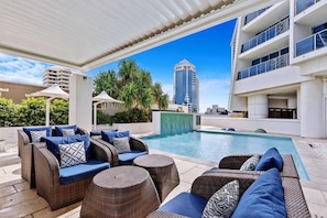 A poolside area with wicker furniture and a view of a tall building.