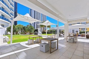 An outdoor patio area with tables and chairs, surrounded by white umbrellas, and a view of high-rise buildings.