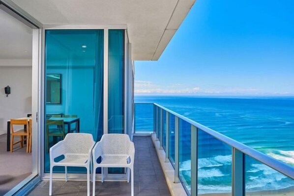A balcony with two white chairs, a table, and a glass door leading to an interior space.