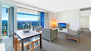 Una habitación de hotel moderna con zona de comedor, sofá, televisor y vista a la ciudad.