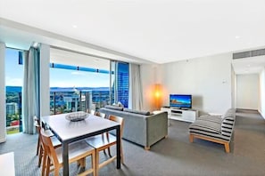 Et moderne hotelværelse med spiseplads, sofa, TV og udsigt over byen.