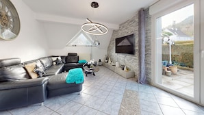 A modern living room with a sectional sofa, a flat-screen TV mounted on a stone wall, and a large window offering a view of the outdoors.