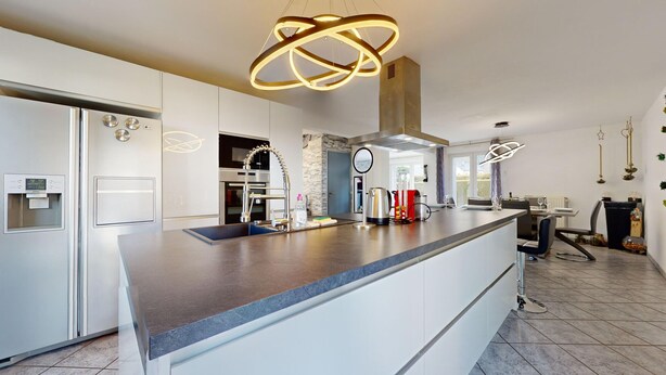 A modern kitchen with a central island, stainless steel appliances, and a unique pendant light.