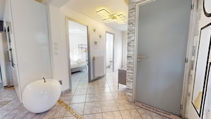 A hallway with a white spherical object, a door with a 'Bonjour & Bienvenue' sign, and a modern light fixture.
