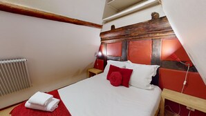 A bedroom with a bed, a red and white pillow, a wooden headboard, a nightstand, a red towel, and a radiator. - Zum Bären Duplex - 1 Parking (Colmar)