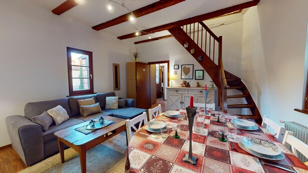 A cozy living room with a sofa, a dining table set with plates and glasses, a staircase, and a view of the outside. - Zum Bären Duplex - 1 Parking (Colmar)