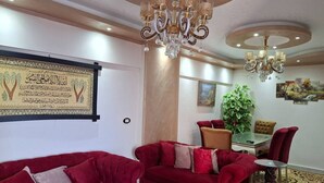 A room with a red sofa, a chandelier, a dining table, and a wall-mounted artwork.