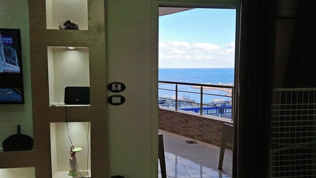 A room with a view of the sea, a balcony with a railing, and a wall-mounted shelf with a statue.