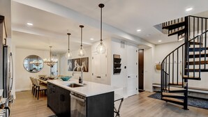 A modern kitchen with a central island, pendant lighting, and a staircase leading to an upper level.
